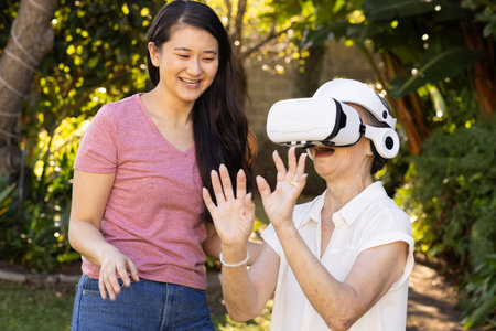 Using VR headset, asian grandmother exploring virtual reality with daughter outdoors. Technology, family, bonding, leisure, seniorの写真素材