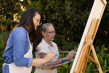 Painting on canvas, Asian granddaughter and grandmother enjoying outdoor art activity together. Artistic, creativity, leisure, relaxation, bonding, hobbyの写真素材