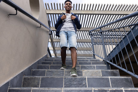 In school, Smiling teenage boy walking down stairs outdoors, carrying backpack. education, campus,...