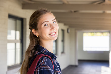 Smiling teenage girl with backpack standing in school hallway, looking at camera. Education, back to school, learning, happiness, youth, academicの写真素材