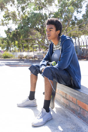 Sitting with skateboard, african american teenage boy relaxing outdoors in casual attire. skateboarding, leisure, youth, lifestyle, relaxation, adventureの写真素材