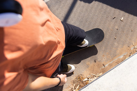 Asian teenage boy skateboarding on pavement, wearing headphones and enjoying outdoor activity. leisure, lifestyle, youth, enjoyment, urbanの写真素材