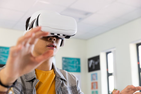 Using VR headset, asian teenage boy exploring virtual reality in school classroom. Education, technology, learning, innovation, immersive, futuristの写真素材