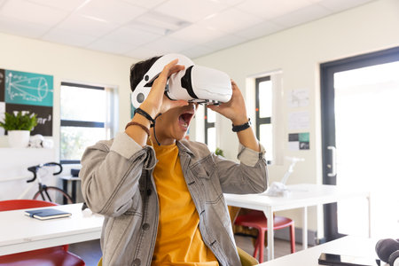 Using VR headset, excited asian teenage boy experiencing virtual reality in school classroom. Technology, education, learning, innovation, experience, excitementの写真素材