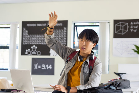 In school, asian teenage boy raising hand while using laptop in classroom. Education, learning,...