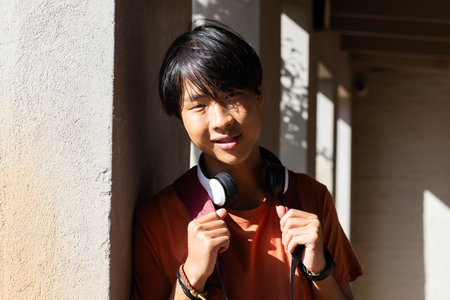 At school, Asian teenage boy with headphones hanging out, smiling and enjoying free time....