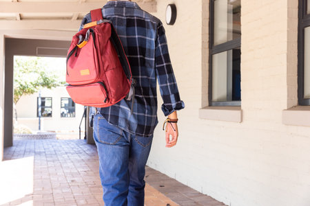 Walking in school hallway, asian teenage boy with red backpack wearing plaid shirt. Education,...
