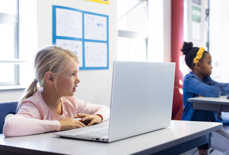 In school, girl using laptop in classroom, focusing on learning activities. Education, technology, studying, childhood, studentの写真素材