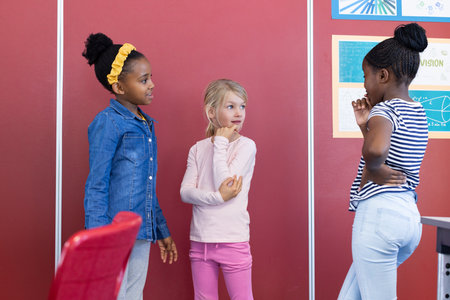 In school, three multiracial girls standing and talking in classroom near posters. education, schoolmates, chatting, teamwork, friendship, studentsの写真素材