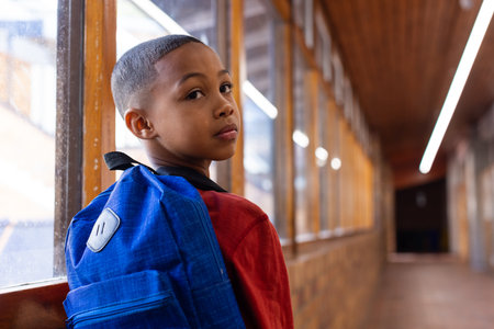 In school, boy with blue backpack looking back in hallway, thoughtful expression. Education, back to school, learning, childhood, studentの写真素材