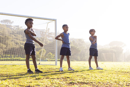 Outdoors, Exercising on school field, three multiracial boys stretching near soccer goal in morning. Fitness, exercise, children, sports, outdoor, teamworkの写真素材