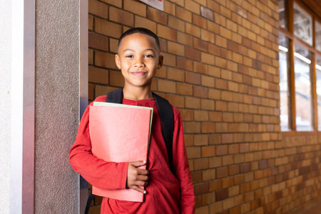Smiling boy holding folder and wearing backpack in school hallway. education, student, childhood,...