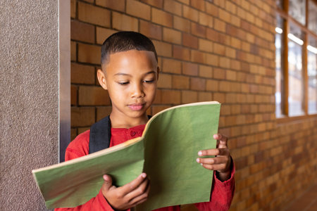 Reading notebook, boy standing in school hallway with backpack on. Education, student, learning,...