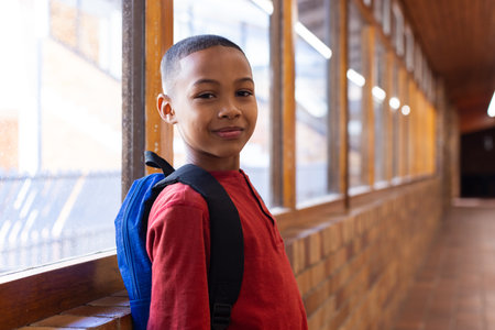 Smiling boy with backpack standing in school hallway, looking at camera. Education, student, childhood, back to schoolの写真素材