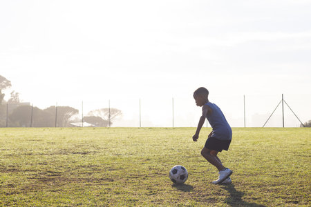 Outdoors, Playing soccer on school field, boy dribbling ball in morning sunlight. sports, children, teamwork, exerciseの写真素材