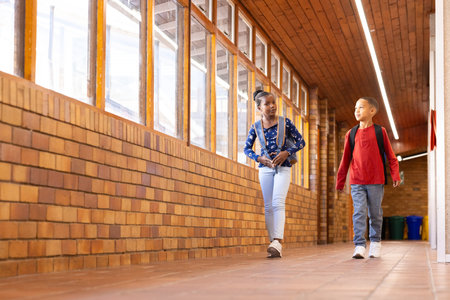 Walking in school hallway, two multiracial boy and girl with backpacks talking and smiling. friends, friendship, conversation, teenagers, happiness, educationの写真素材