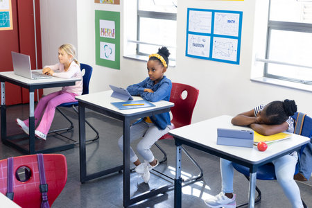 In school, multiracial girls using tablets and laptop in classroom, studying attentively....