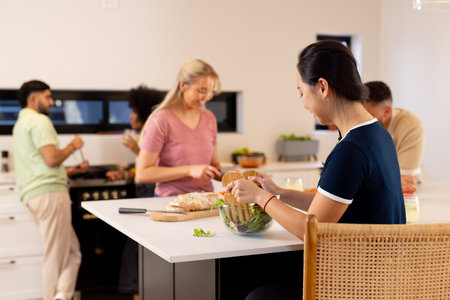 Preparing food together, group of young diverse friends enjoying time in kitchen. Cooking, diverse friendship, togetherness, meal preparation, fun, bondingの写真素材