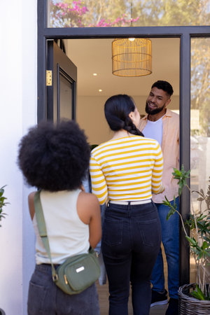 Greeting friends at doorway, man smiling and welcoming two women into home. Welcome, friendship,...