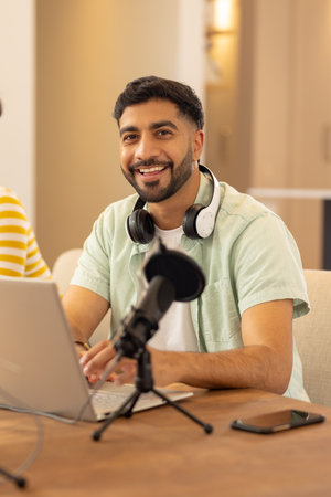 Using laptop and microphone, man smiling while working from home office. Remote working, technology, freelancer, virtual, business, communicationの写真素材
