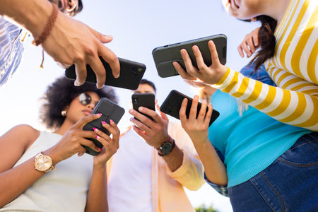 Group of diverse friends holding smartphones, sharing and discussing content outdoors. socializing,...