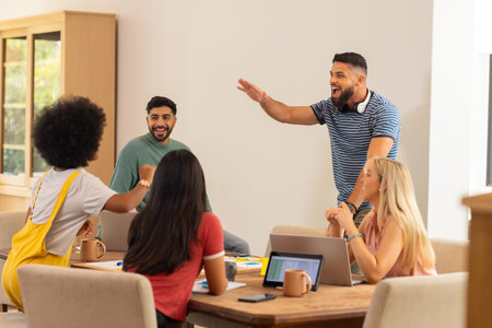Group of young friends laughing and high-fiving while working on laptops, start up business....