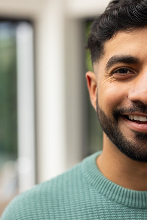 Smiling Indian man in green sweater enjoying time indoors, close-up portrait, copy space. happiness, comfort, cheerful, male, relaxationの写真素材