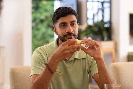 Eating snack, man sitting at table and enjoying casual conversation indoors. Food, dining, enjoymentの写真素材