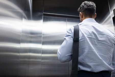 Businessman with shoulder bag standing in elevator, commuting to work, copy space. professional, office, corporate, transportation, urban, lifestyleの写真素材
