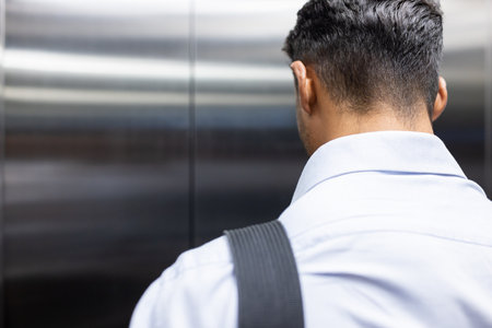 Businessman in elevator facing wall, wearing formal shirt and shoulder bag, copy space. Corporate,...