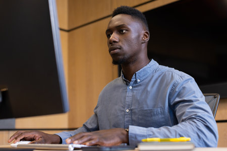 Working on desktop computer, man focusing on tasks in modern office. professional, business,...
