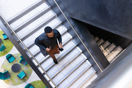 Walking up stairs, businessman holding smartphone and coffee cup in office building. corporate, professional, technology, mobile, rush, busyの写真素材