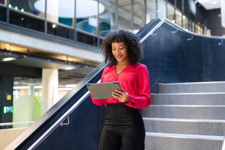 Using tablet, businesswoman standing on stairs in modern office building. technology, professional,...