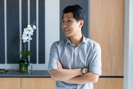Confident asian man standing with arms crossed in modern office space. confidence, professional, workplace, corporate, leadership, executiveの写真素材