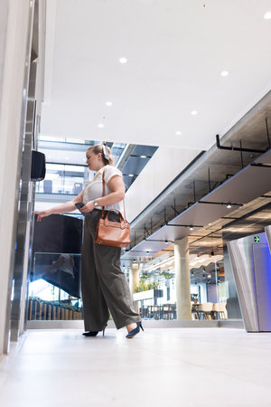 Pressing elevator button, businesswoman in office holding tablet and handbag. corporate,...