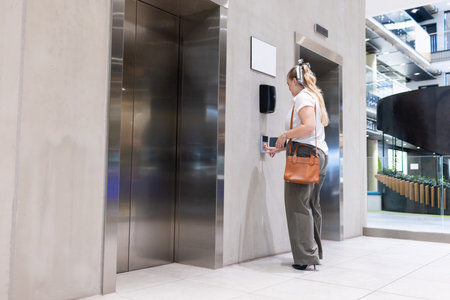 Pressing elevator button, businesswoman in modern office building lobby. corporate, technology,...