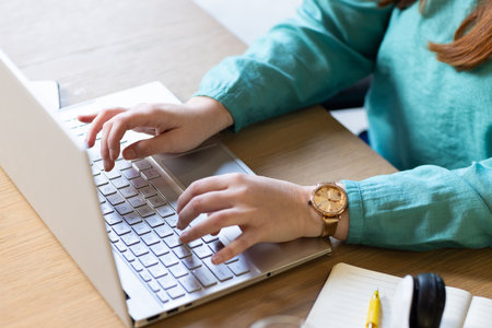 At office, typing on laptop, woman working with notebook and pen nearby. remote working, office,...