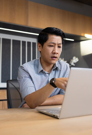 Working on laptop, asian man in office focusing on business tasks. workplace, concentration,...