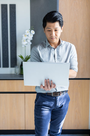 Working in modern office, asian man holding laptop and focusing on task. Business, technology, productivity, professional, computer, corporateの写真素材