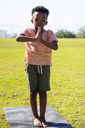 Practicing yoga, young african american boy standing on yoga mat in outdoor setting. exercise, fitness, child, wellness, meditation, outdoorsの写真素材