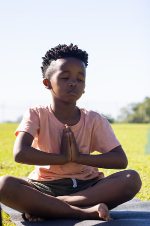 Meditating on yoga mat, african american boy practicing mindfulness outdoors in school setting....