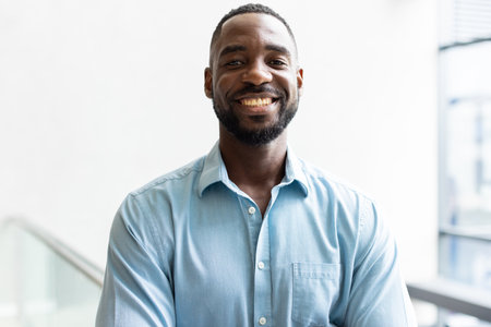 Smiling african american man in blue shirt standing confidently in modern office environment. Business, professional, workplace, corporate, executive, entrepreneurの写真素材