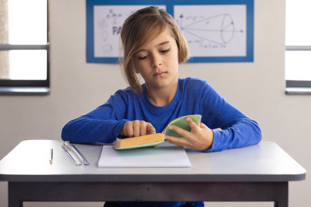 In school, boy reading book at desk, focusing on learning in classroom. Education, back to school,...
