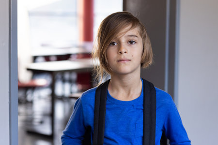 In school, boy wearing backpack standing in classroom, looking at camera. Education, back to school,...