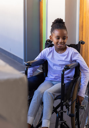 In school, african american girl in wheelchair smiling and looking ahead in hallway. Education, inclusivity, empowerment, positivity, accessibilityの写真素材