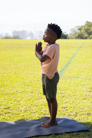 Outdoors, Practicing yoga, young african american boy standing on yoga mat in school field....