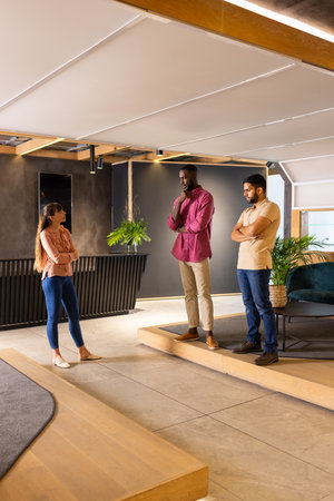 Discussing project ideas, three colleagues standing in modern office space. Teamwork, collaboration,...