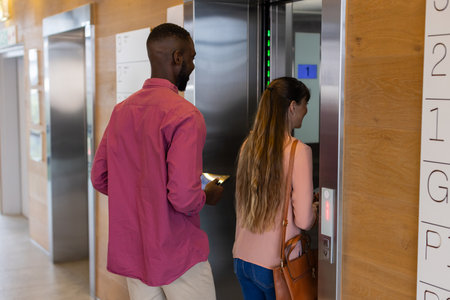Entering elevator, man holding smartphone and woman pressing button, office setting. Business, corporate, technology, colleagues, professional, convenienceの写真素材