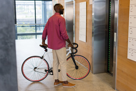 Man holding bicycle waiting for elevator in modern office building lobby. Urban, transportation,...