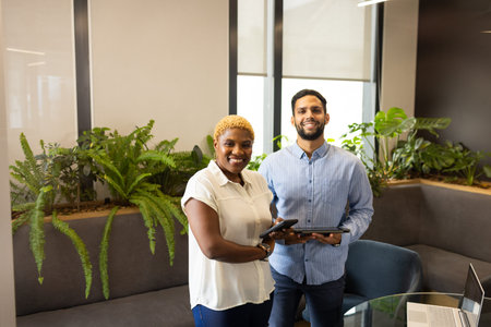 Smiling colleagues holding tablets in modern office with indoor plants. Business, teamwork,...